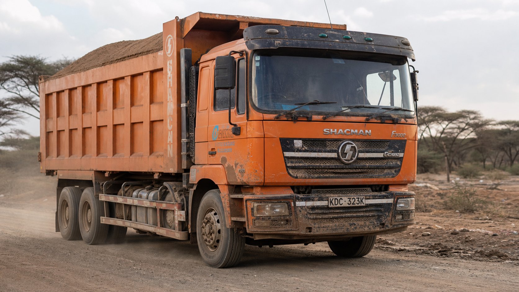 Dirty orange Shacman tipper truck KDC 323K loaded with murram on Kenyan road
